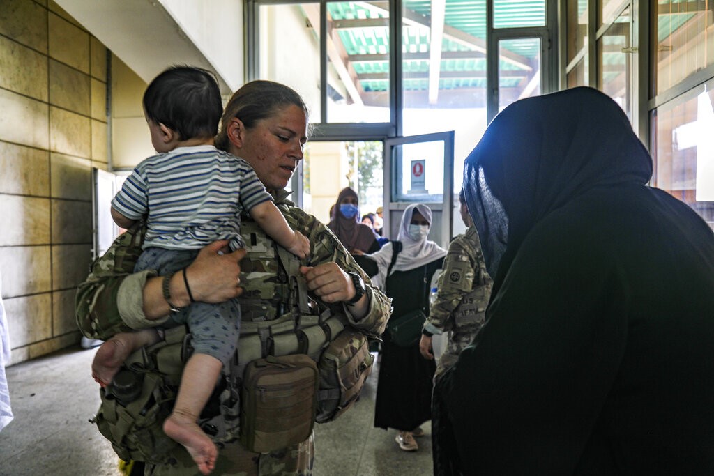 In this image provided by the U.S. Army, a medical officer assigned to the 82nd Airborne Division speaks with an Afghan woman and helps her with her child during ongoing non-combatant evacuation of U.S. civilian personnel, Special Immigrant Visa applicants, and other at-risk individuals, at Hamid Karzai International Airport, Kabul, Afghanistan, Wednesday, Aug. 25, 2021. (Sgt. Jillian G. Hix/U.S. Army via AP)